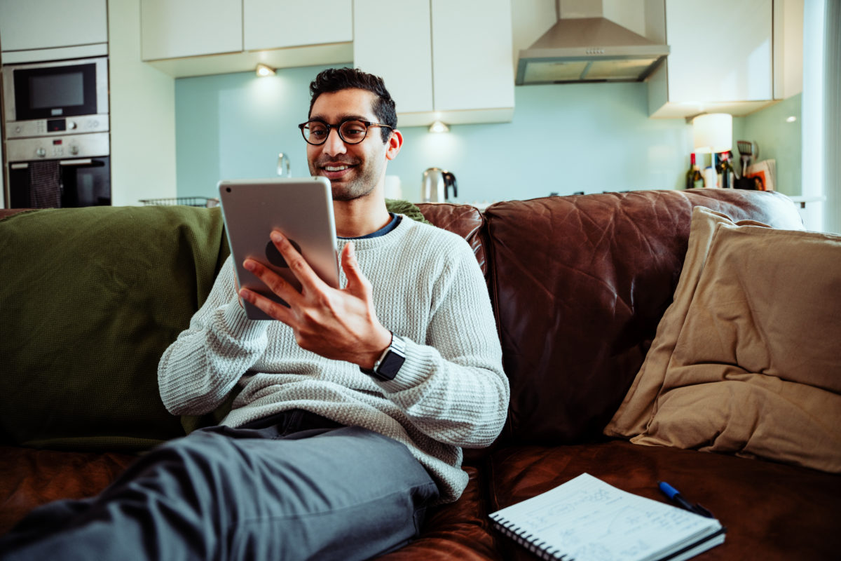 Uomo seduto sul divano che usa il suo tablet