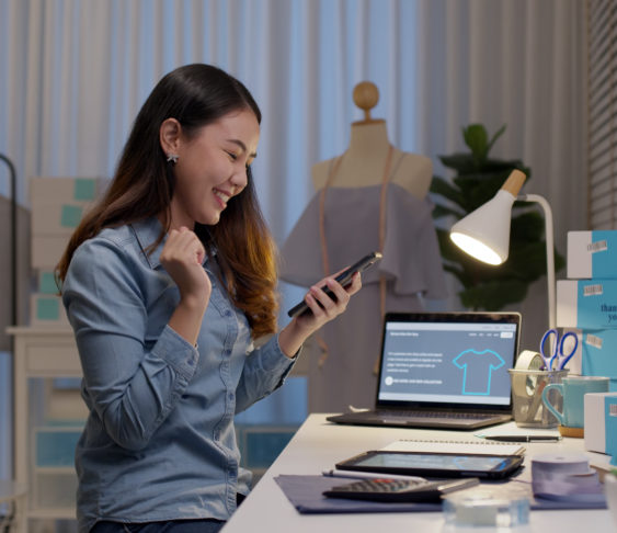 Woman looking at her phone with excitement while sitting at her desk.