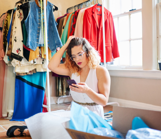 Seller checking their phone with clothes on a rack in the background